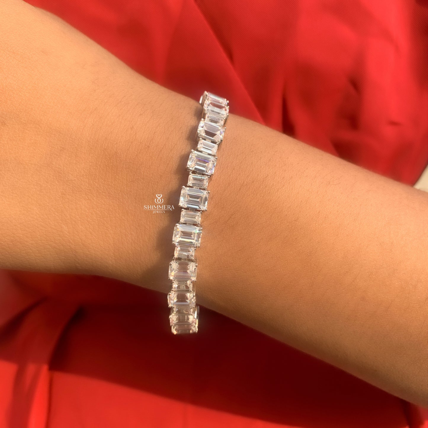 Silver bracelet with baguette-cut diamonds on a wrist against a red background, featuring the Shinnara Jewelry logo.