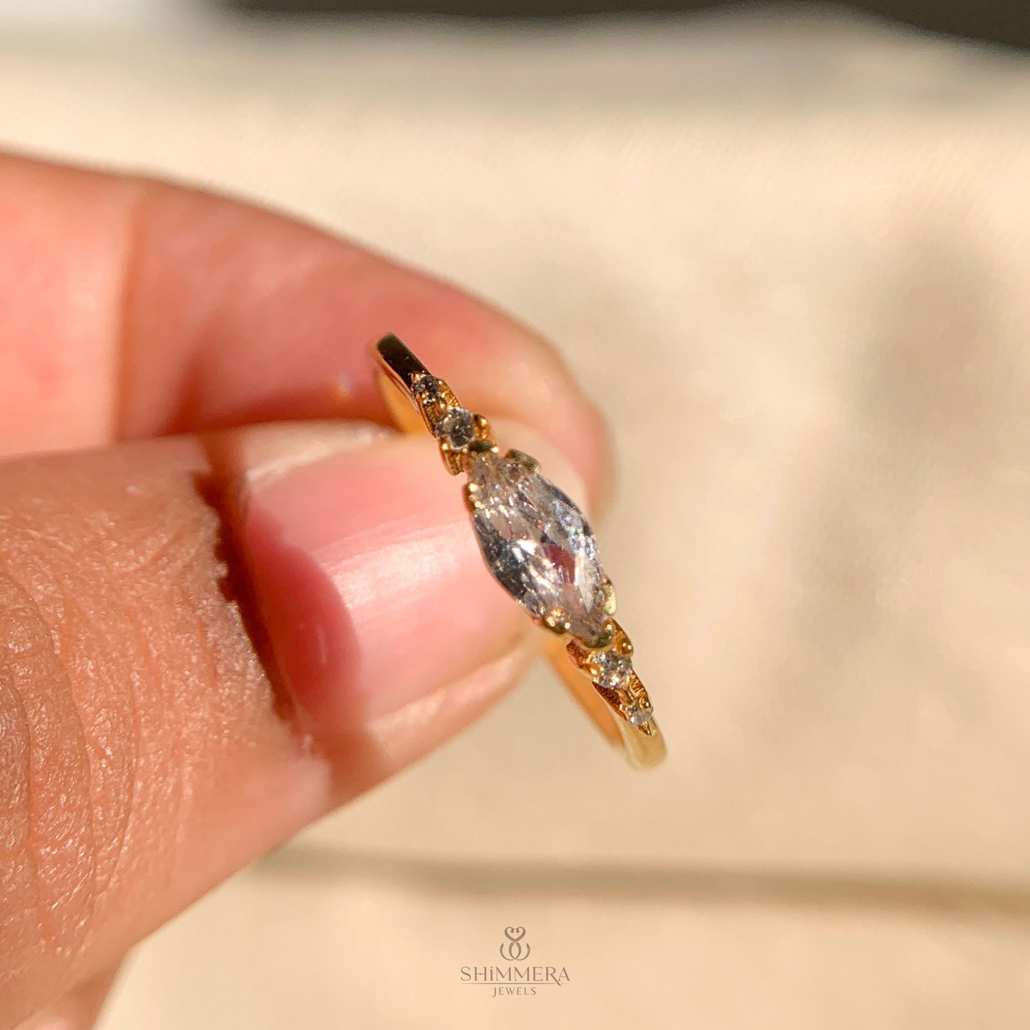 Gold ring with a diamond held between fingers, Shimmera Jewels logo visible
