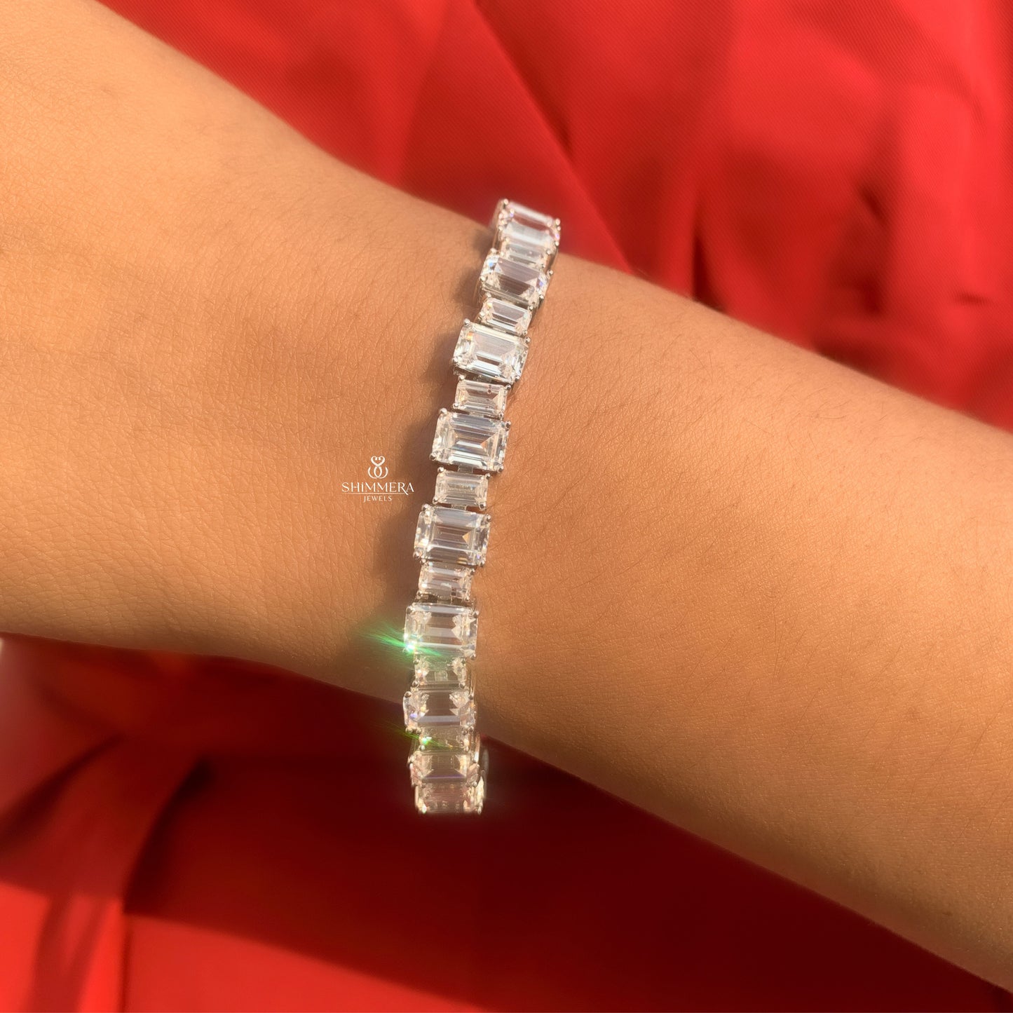 Silver bracelet with baguette-cut diamonds on a wrist against a red fabric background