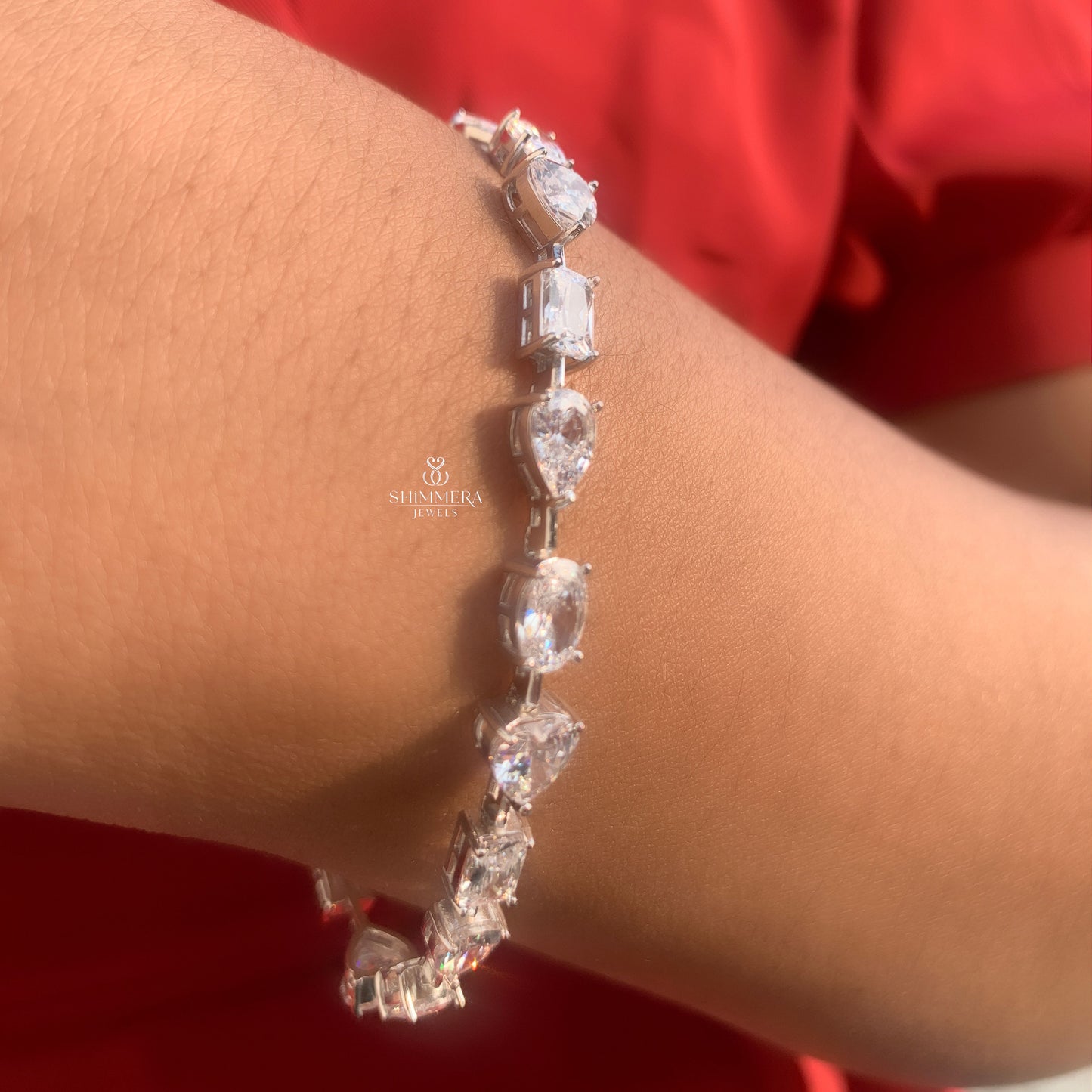 Silver bracelet with clear stones on a wrist against a red background