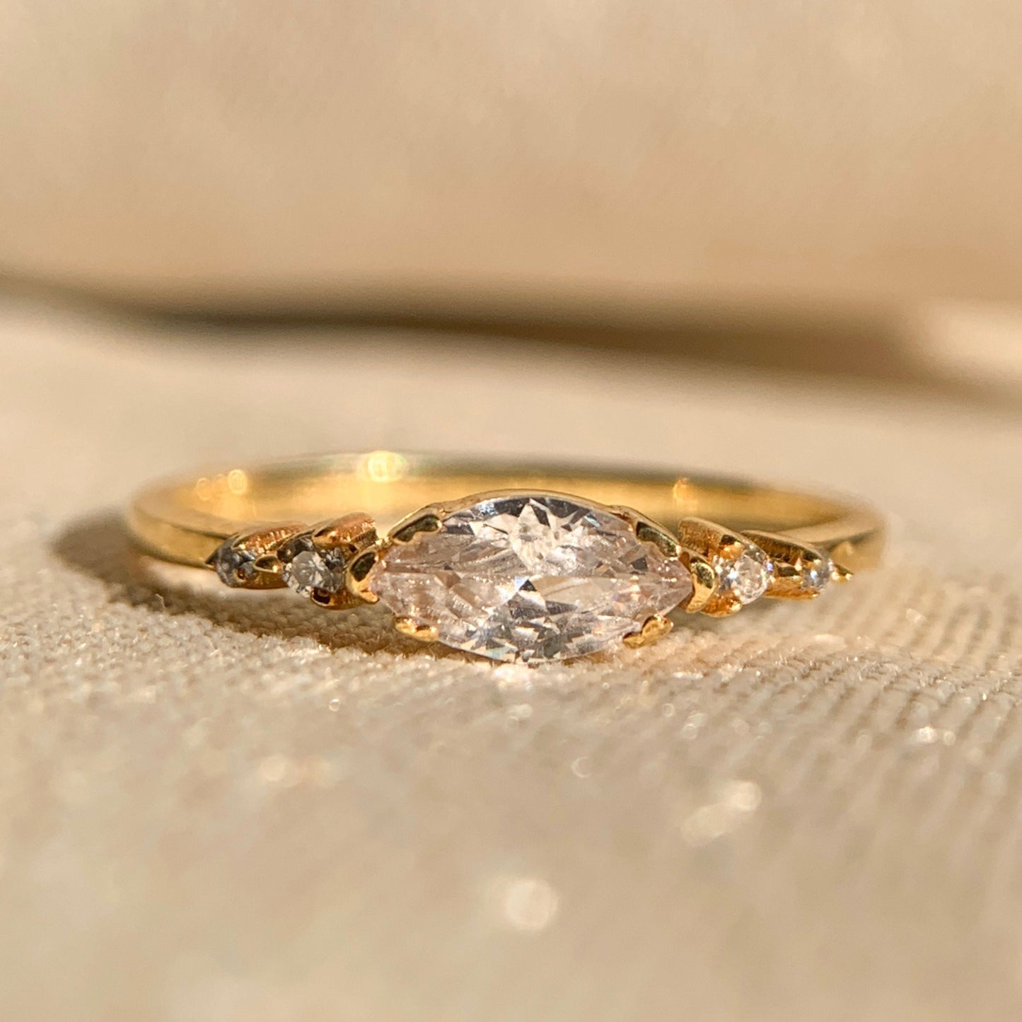 Gold ring with a large diamond and smaller stones on a beige background
