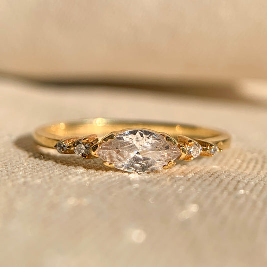 Gold ring with a large diamond and smaller stones on a beige background