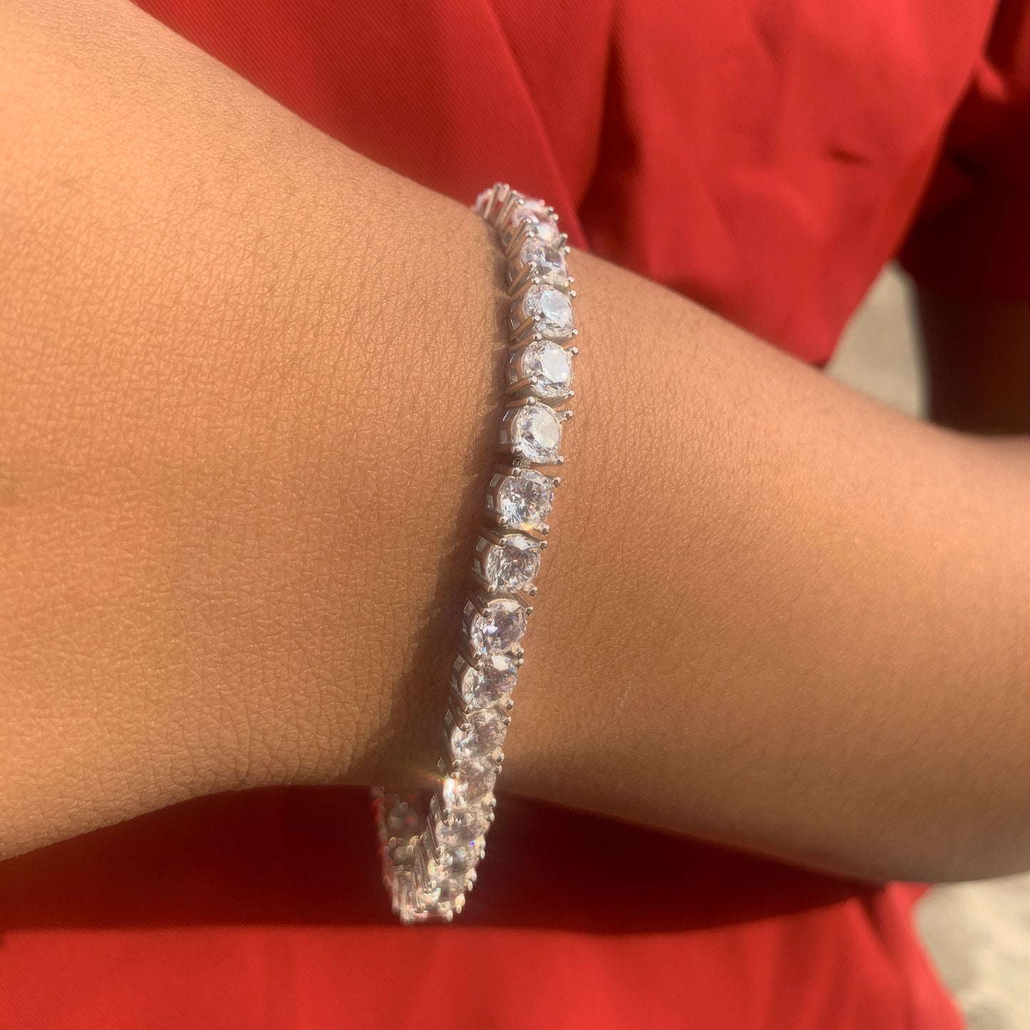 Silver bracelet with clear stones on a wrist against a red background