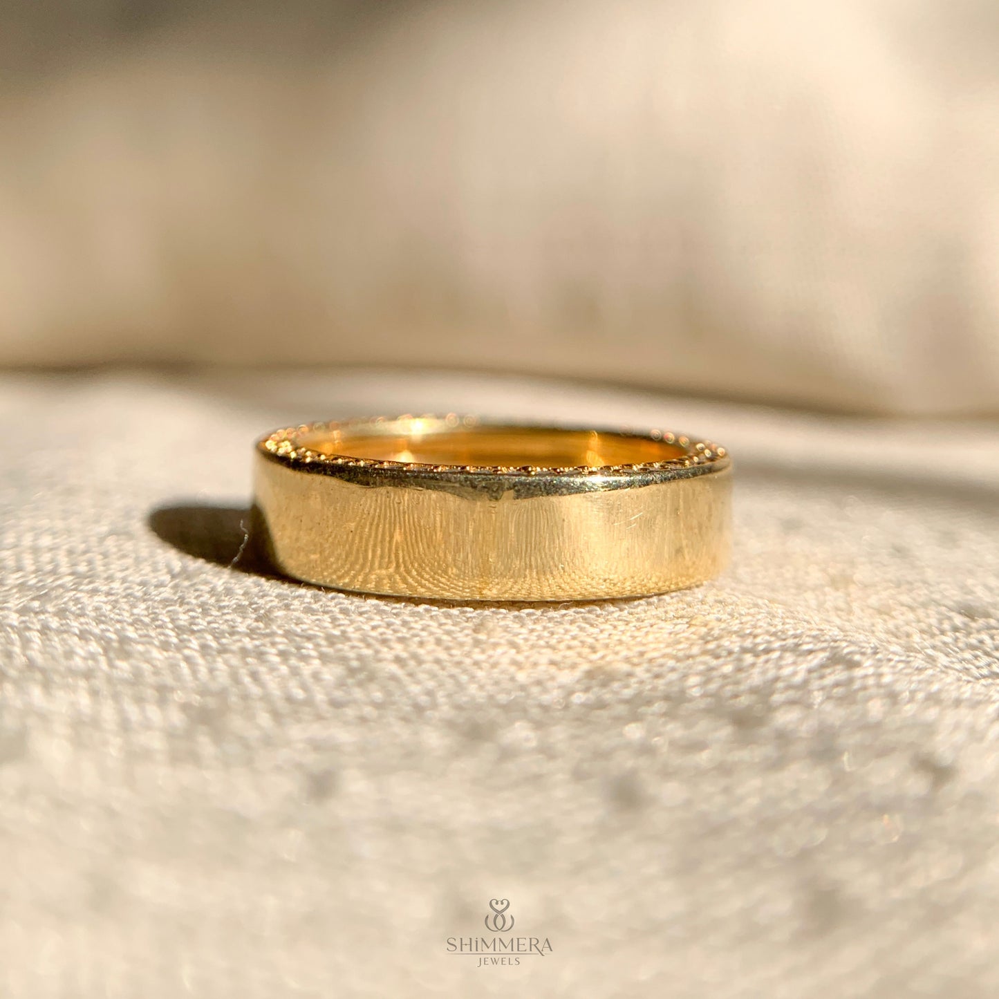 Gold ring on a textured beige surface with 'Shimmera' branding.