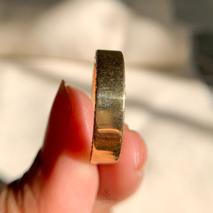 Gold ring held between fingers with a blurred background