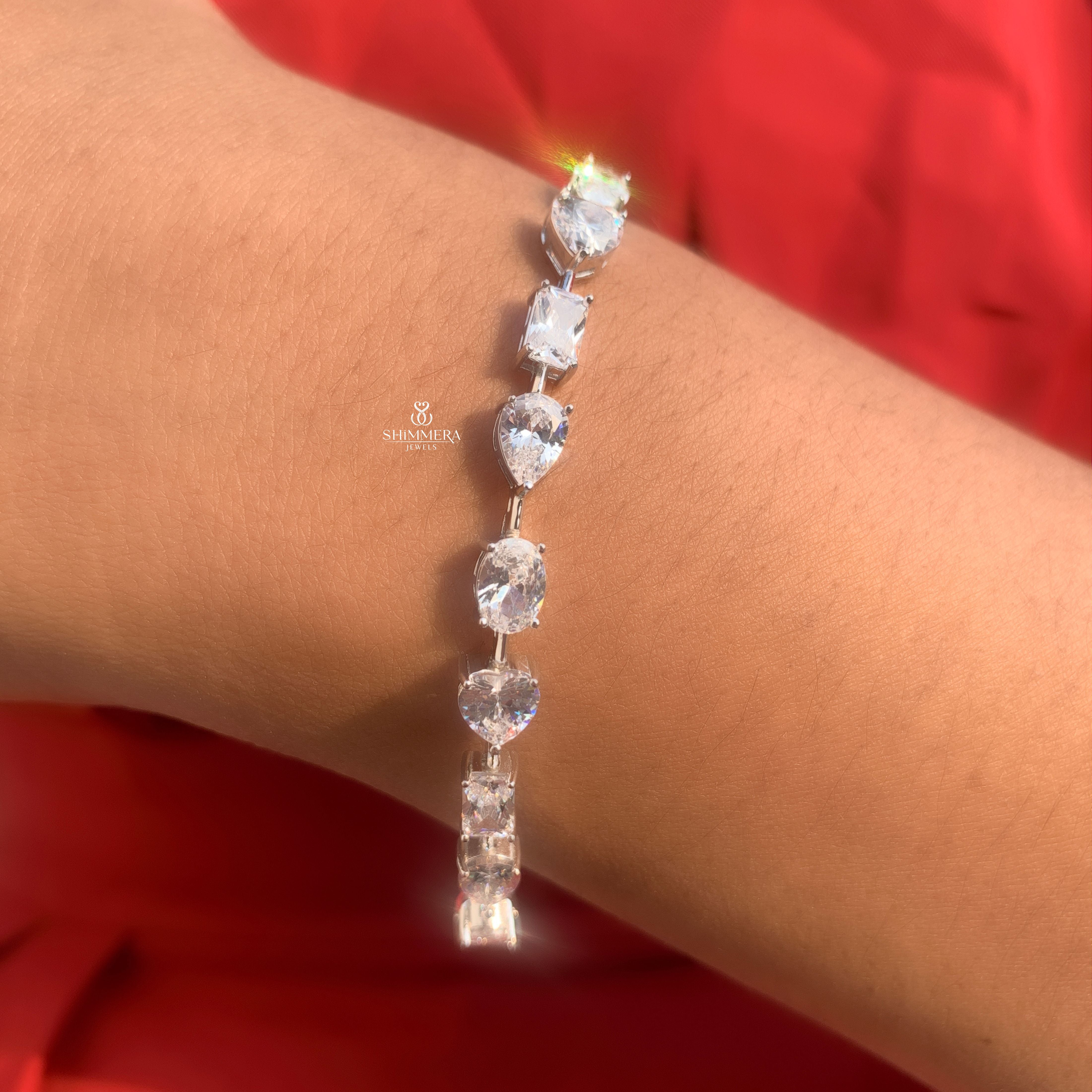 Silver bracelet with clear stones on a wrist against a red background