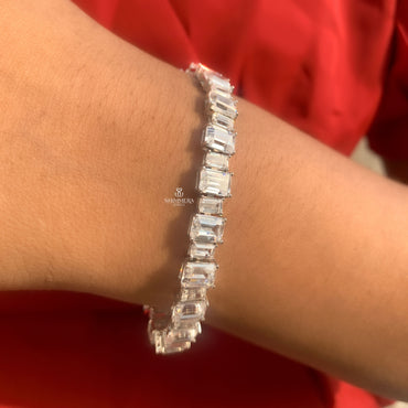Silver bracelet with emerald-cut stones on a wrist against a red background