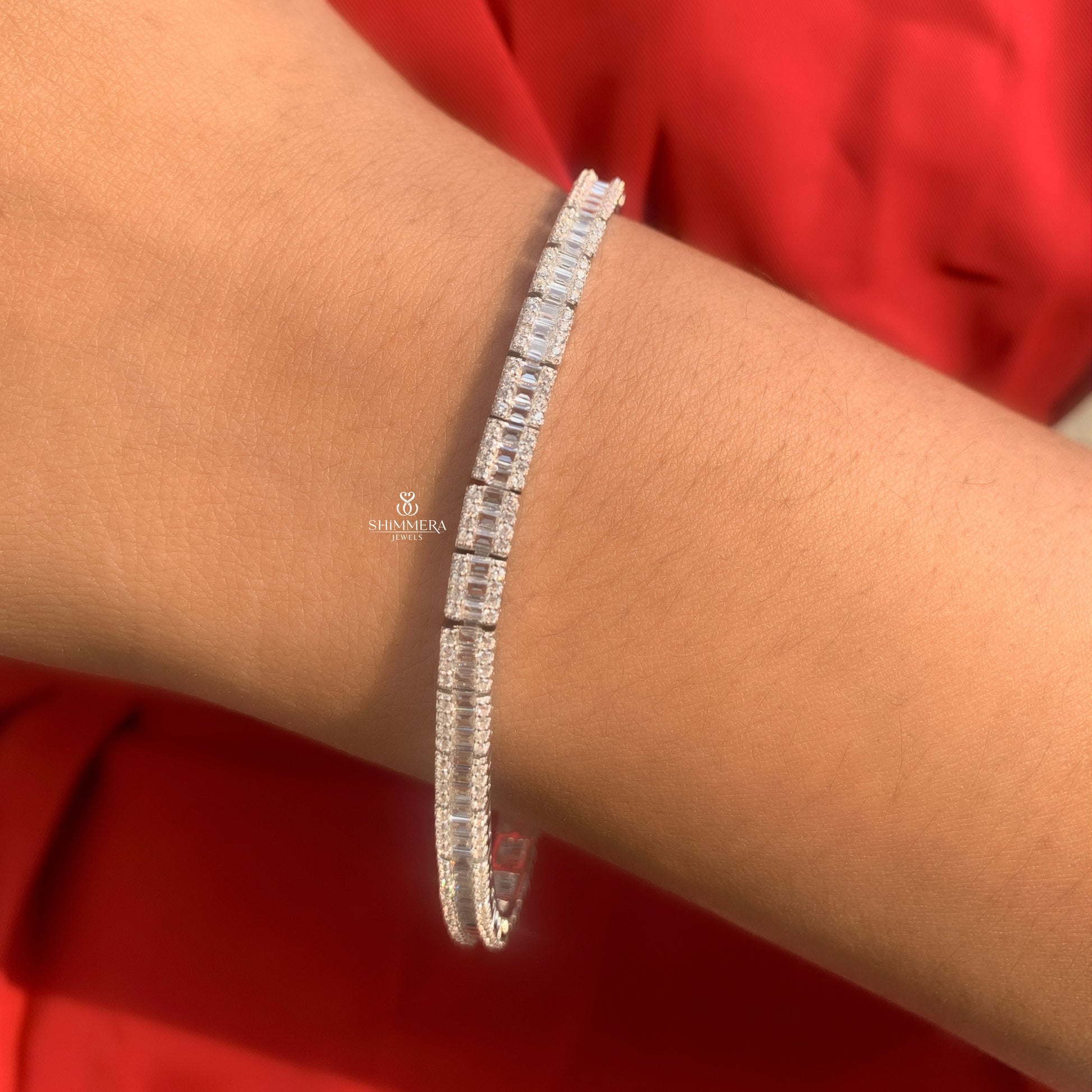 Silver bracelet with clear stones on a wrist against a red background