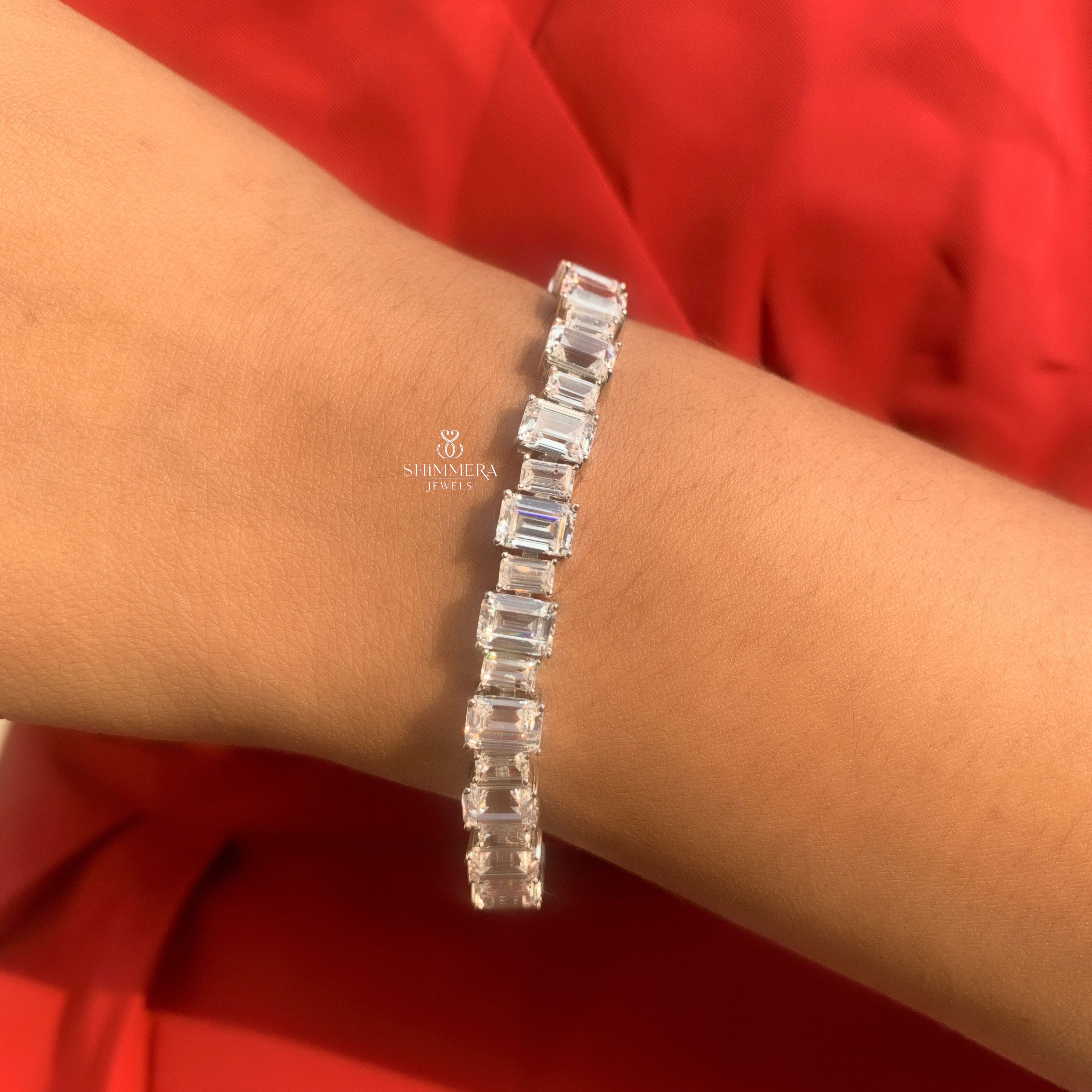 Silver bracelet with rectangular crystals on a wrist against a red background