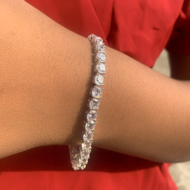 Silver bracelet with clear stones on a wrist against a red background